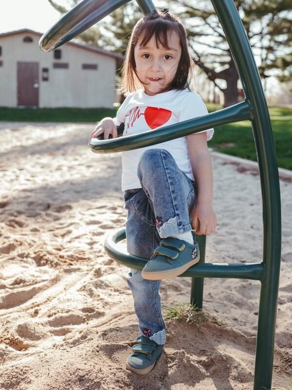 A full body image of a young girl playing at a park wearing Mukishoes bee barefoot sneakers