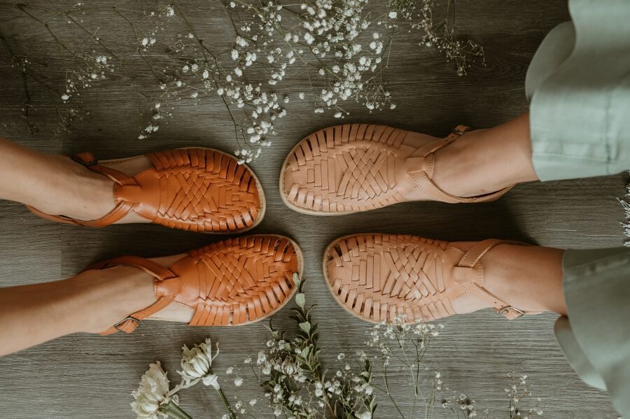 top down view of Origo Huarache Sandals in regular and wide width. Flowers are scattered around the ground, and the woven leather in nutmeg and tan is in the center of the image.