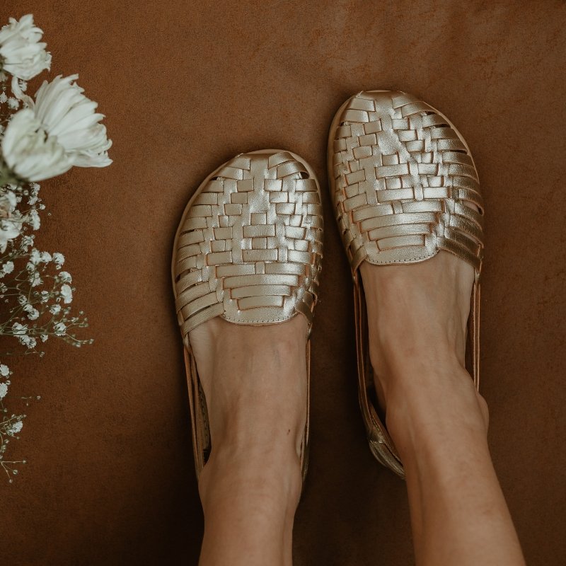 Origo Huarache slip-on flats in gold leather with a wide anatomical toe box for comfortable all day wear. A bouquet of white flowers is showing on the side