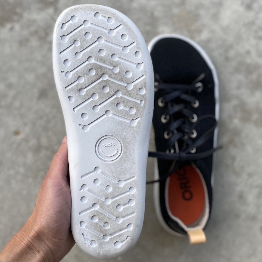 a close up of a hand holding an Origo Shoes affordable barefoot sneaker with the sole facing up to show it's natural foot shape