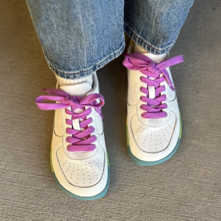 Top down close up of a pair of sneakers with bright pink laces, a wide toe box, and colorful outsoles.