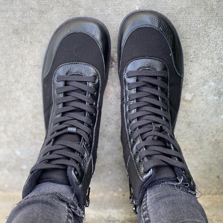 A top down view of a pair of feet standing on concrete wearing black PaperKrane Snugg barefoot combat boots