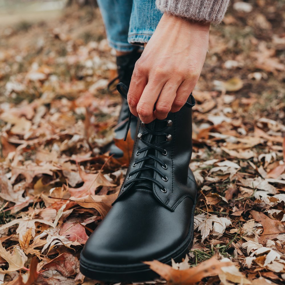 Close up of the front barefoot wide toe box of a person adjusting the laces on a pair of Peerko Frost black lace up leather winter boots