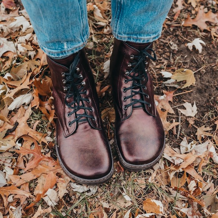 A top view of a pair of feet standing in leaves wearing Peerko Frost barefoot winter boots in Chestnut color