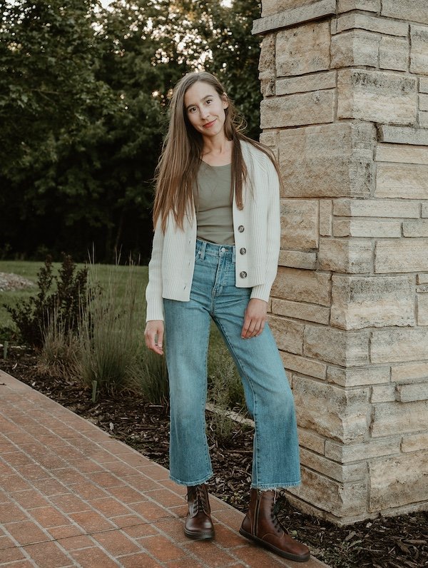 A woman standing outside on brick wearing wide leg jeans and brandy brown leather Peerko Go barefoot wide toe box combat boots