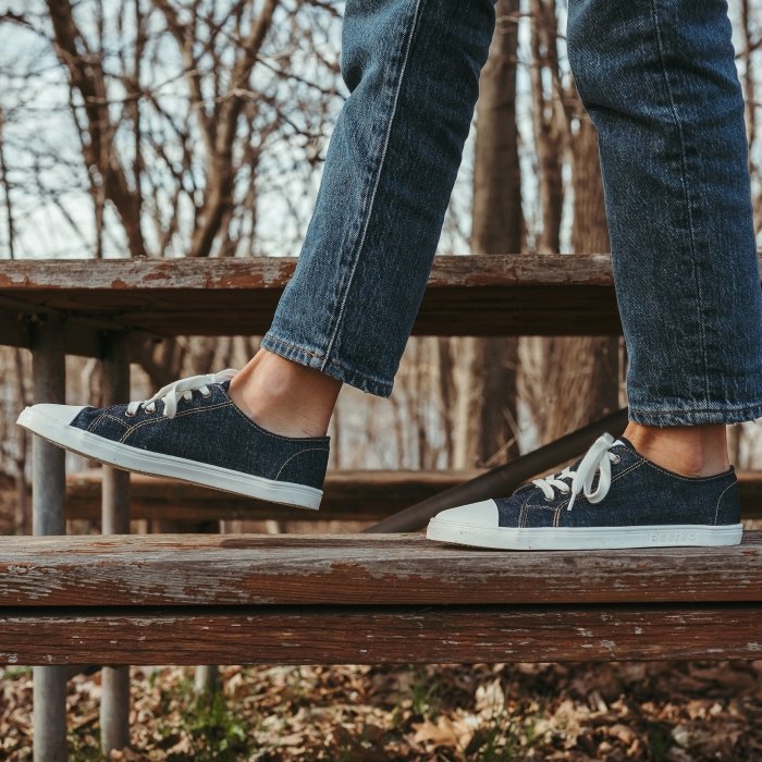 A pair of legs walking on a bench outside in the fall. She is wearing Peerko Origin canvas barefoot sneakers that look like converse
