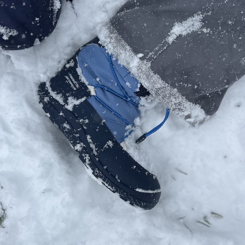 A close up of a pair of Reima Ensilumi barefoot winter boots being worn by a young child in deep snow