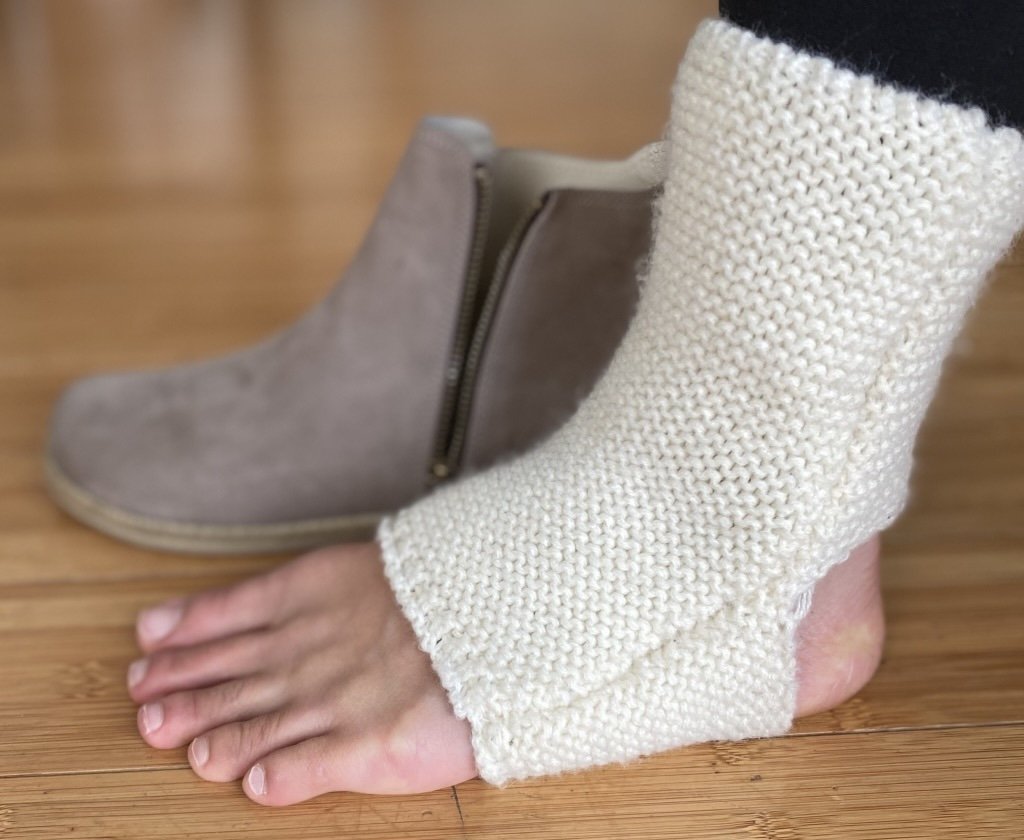 A close up of a person's foot wearing leg warmers next to a barefoot boot, the Rosa by Anya