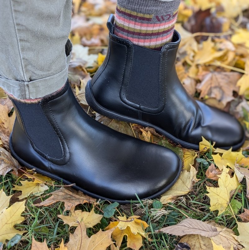 Side flexed view of Saguaro Urban, a non-leather smooth black barefoot chelsea boot. A striped colorful sock is shown above the back boot