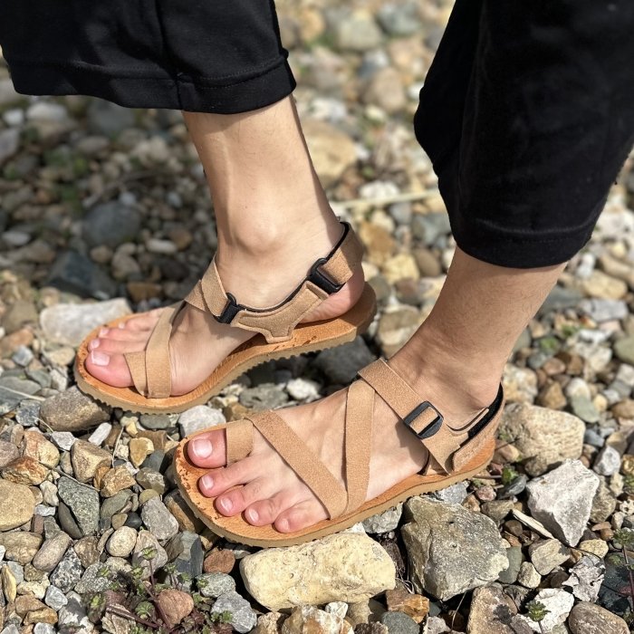 A person in Shamma Sandals Trail Star sandals in tan leather standing on rocky ground with the back foot flexed up