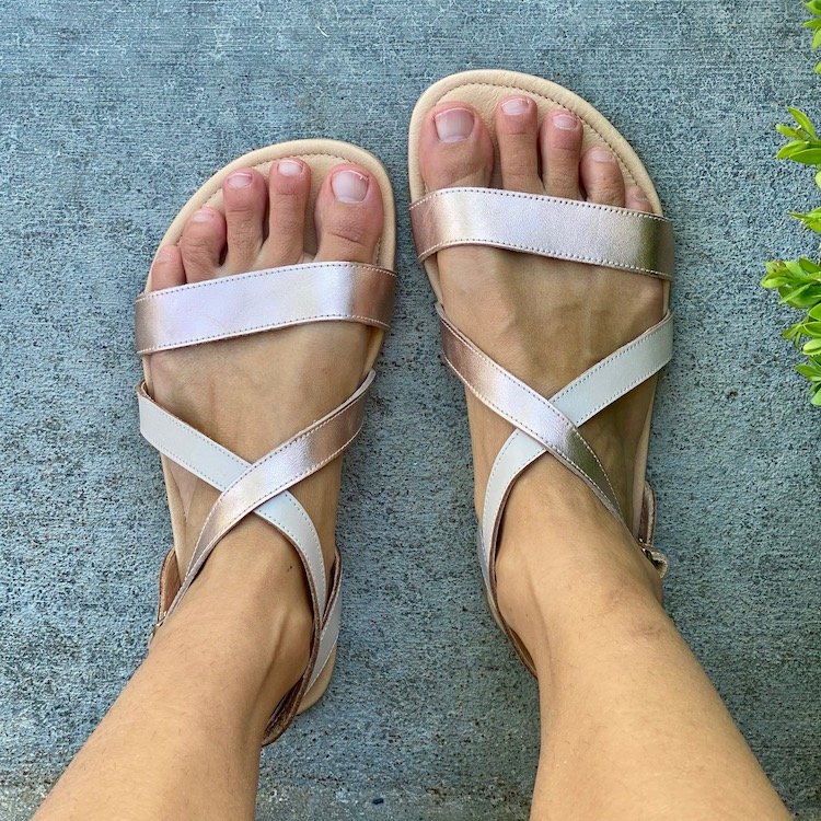 A top down view of a pair of feet standing on concrete wearing Shapen Barefoot Calla Sandals in Rose gold