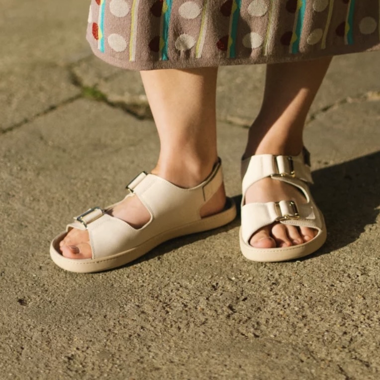 Close up photo of a person's feet in Shapen Dazzle double buckle sandals in shiny cream leather