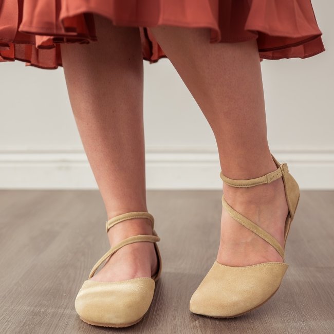 A close up of a woman's legs wearing a peachy brown pleated skirt and Shapen Barefoot Orchid dressy barefoot flats with diagonal strap in tan suede