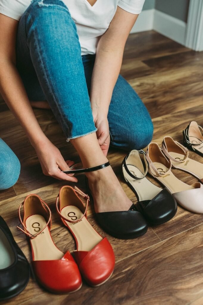 A row of stylish and chic barefoot dress shoes called the Shapen Poppy in regular and wide width with a woman's foot putting the shoe one