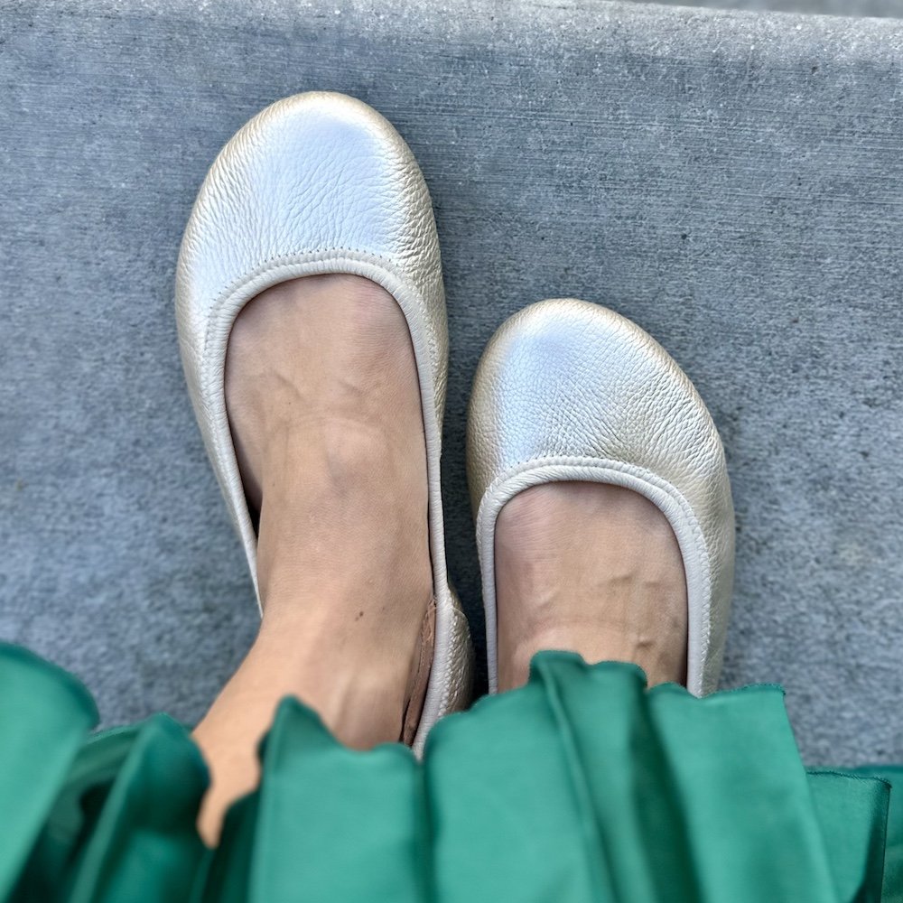 Close up top down view of Softstar Ballerine metallic handmade sustainable barefoot ballet flats. A pleated green dress is visible near the legs