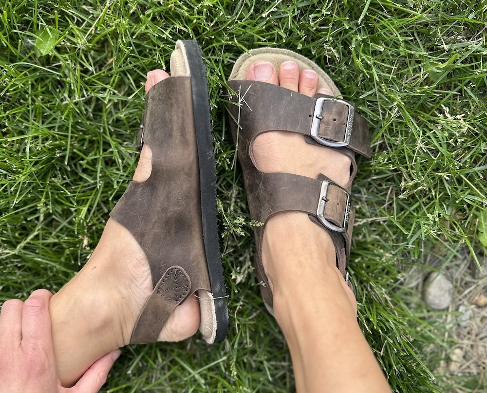Top down and side view of Softstar Camino minimalist sandals with a cushioned insole being worn by a person with wide feet on grass. The zero drop rubber sole is moderately thick.