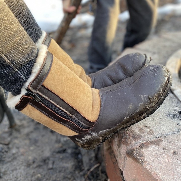 Side view of Softstar Shoes Phoenix boots resting on a firepit. the soles are muddy, but they look warm and cozy.