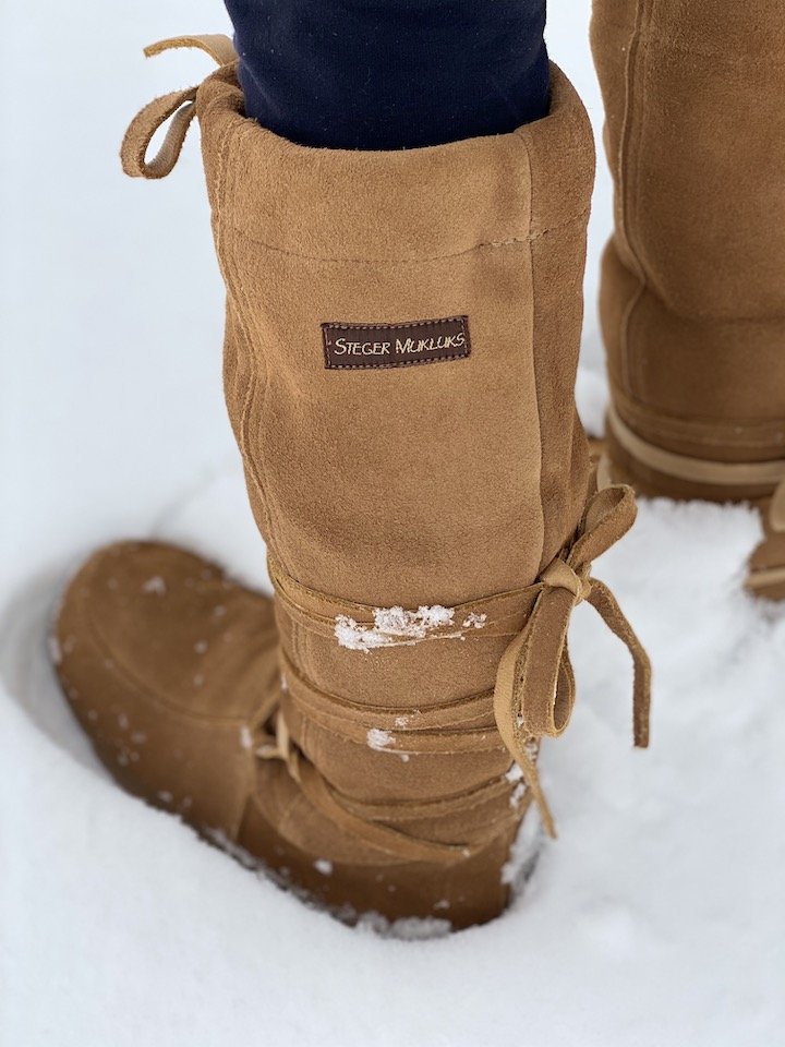 A pair of legs standing in deep snow wearing a pair of wrap around warm Steger Mukluks winter boots