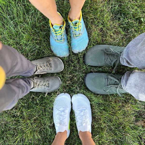 A top down view of a family of 4 all wearing stretchy knit barefoot shoes. Saguaro, Vivobarefoot, Freet, and Reima are all the brands with wide toe box knit shoes