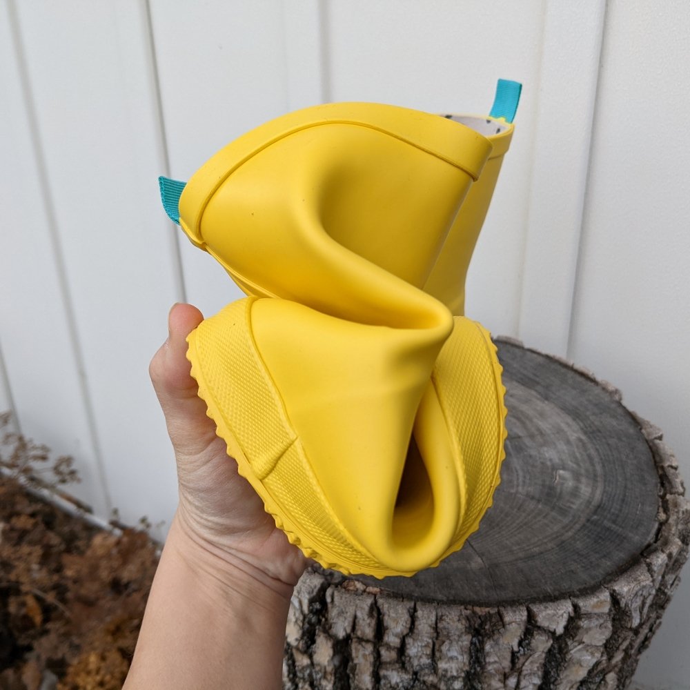 A hand squishing a Ten Little Rain Boot to show how very flexible they are