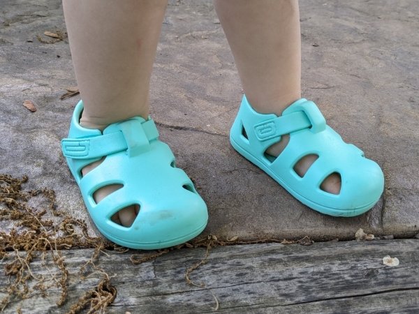 Ten Little Splash sandals in an aqua green color being worn by a toddler. The wide toe box is at the forefront of the image and they are being worn as a barefoot replacement for Crocs for toddlers