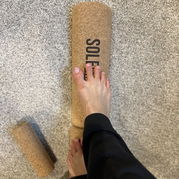 A top down view of a person standing on a cork balance beam with barefoot. Balance beam is the foot collective Solemate