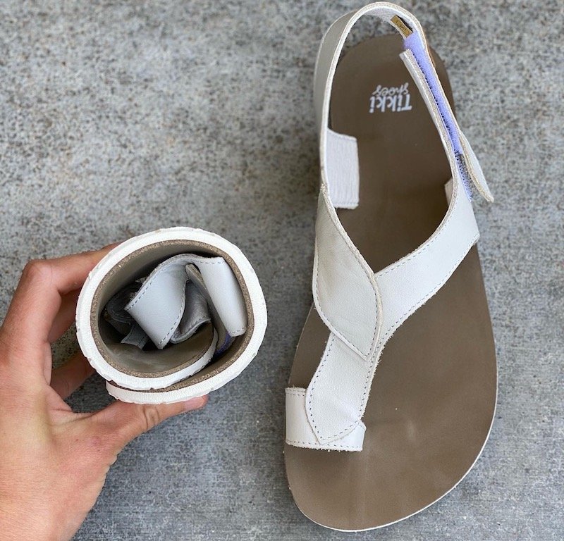 A pair of white Soul Tikki Shoes barefoot sandals for women with one rolled up into a ball to show its flexibility and the other showing the natural foot shape of the sole