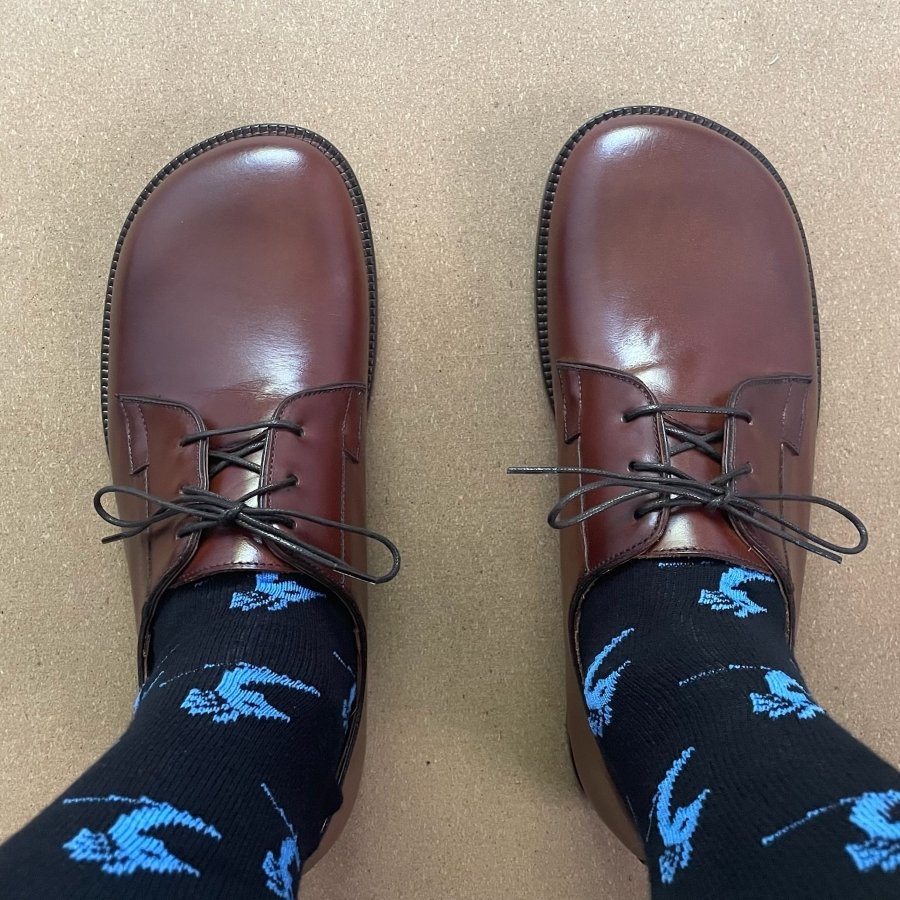 Top down close up view of patterned socks and Tomas Sullivent wide toe box brown leather Italian made dress shoes for men.