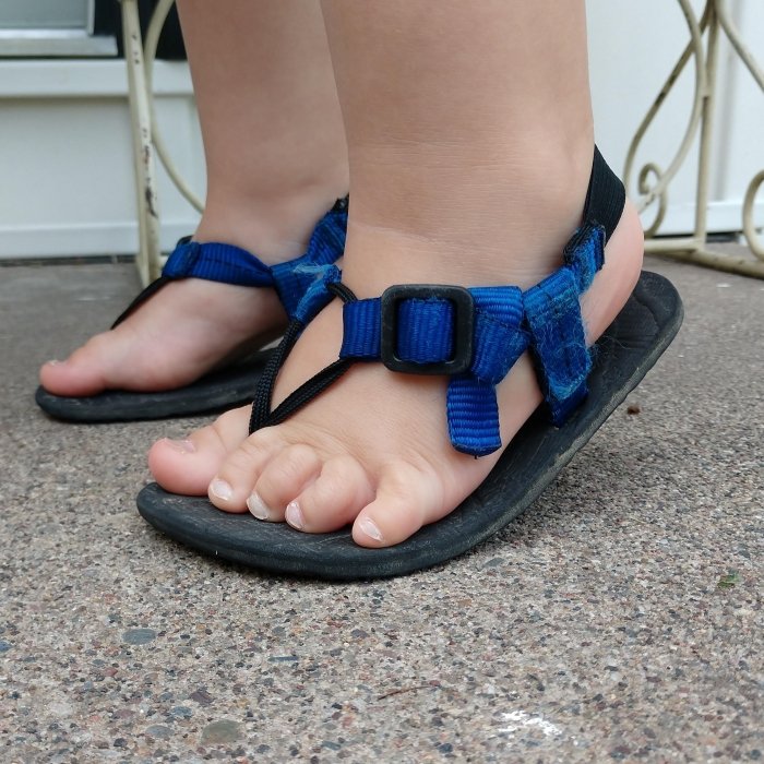 A toddler flexing their feet in Unshoes Keota sandals to show the easy flexibility of these barefoot sandals