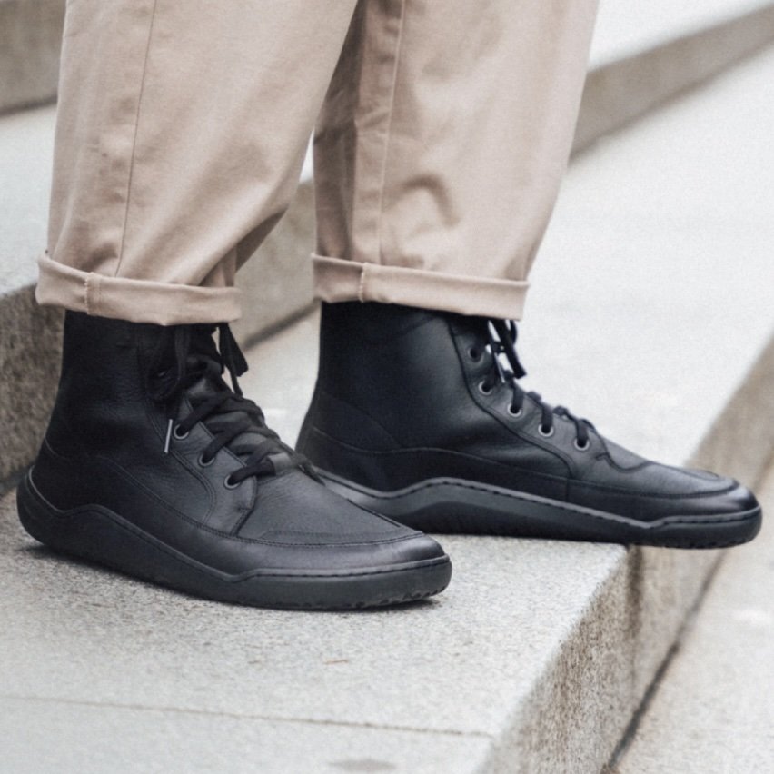 A close up side view of a pair of man's feet wearing the Vivobarefoot Gobi Hi black barefoot combat boot for men