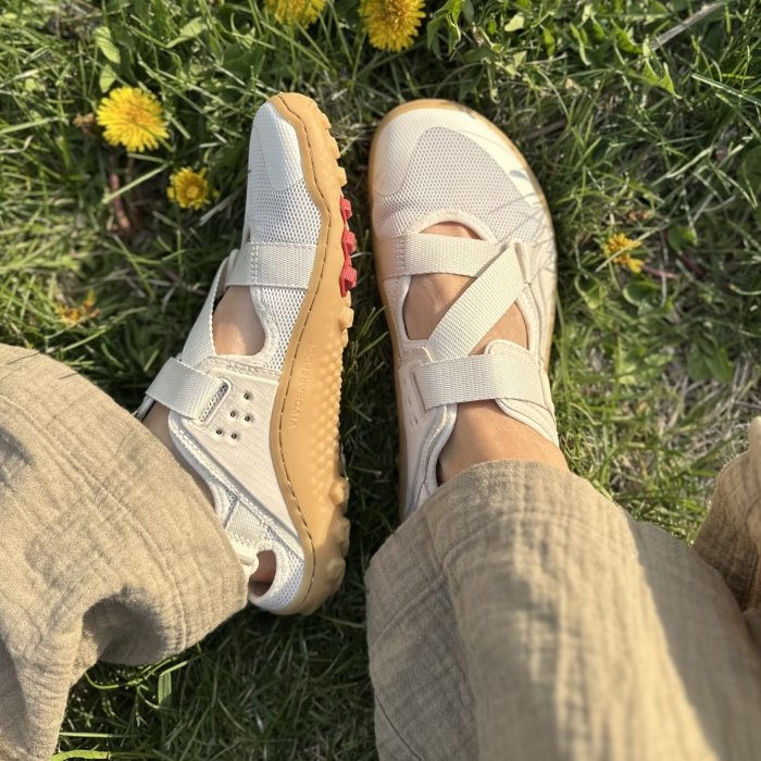 A top down and side view of Vivobarefoot Tracker sandals in white on grassy ground with dandelions