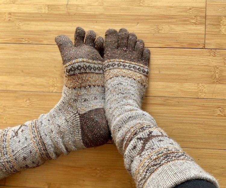 A pair of feet wearing thick cozy wool toe socks with wintry prints on them resting on a wood floors