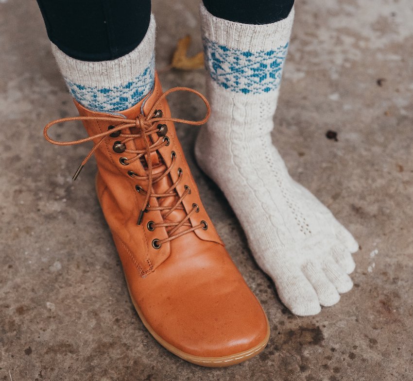 a close up side view of a pair of feet standing on concrete wearing wool knitido toe socks with lace up barefoot boots