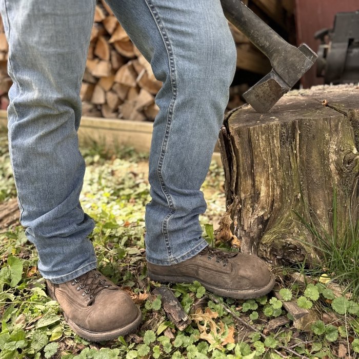A man in jeans shown from the thigh down chopping wood wearing zero drop Carets Determination Steel Toe Safety boots with a wide toe box