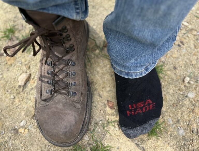 Top down close up view of a man with 1 Carets Determination Safety steel toe boot on, and one socked foot to show the wide toe box that won't squish toes