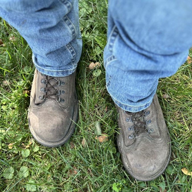 Top down view of wide toe box steel toe work boots with a zero drop rugged outsole. The Carets Determination Steel toe box is being worn by a man in jeans standing on grass.