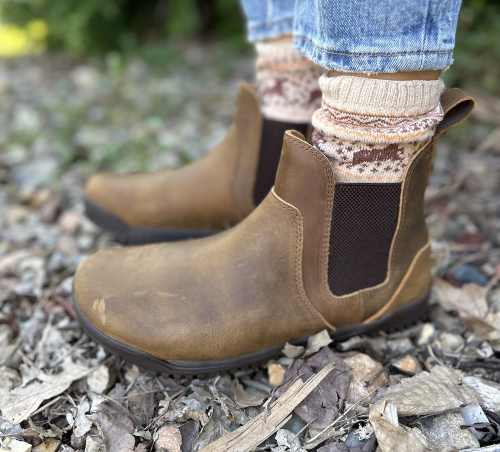 a close up of the new Xero barefoot shoes ridgeway chelsea boot in brown leather on a woman's feet fromt he side standing outdoors