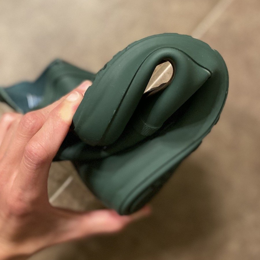 a hand holding a rolled up green Xero Shoes Gracie rubber rain boot to show its flexibility