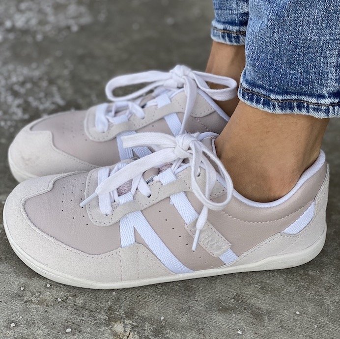 A side view of a pair of feet standing on concrete wearing the Xero Shoes Kelso barefoot sneaker made of pink leather