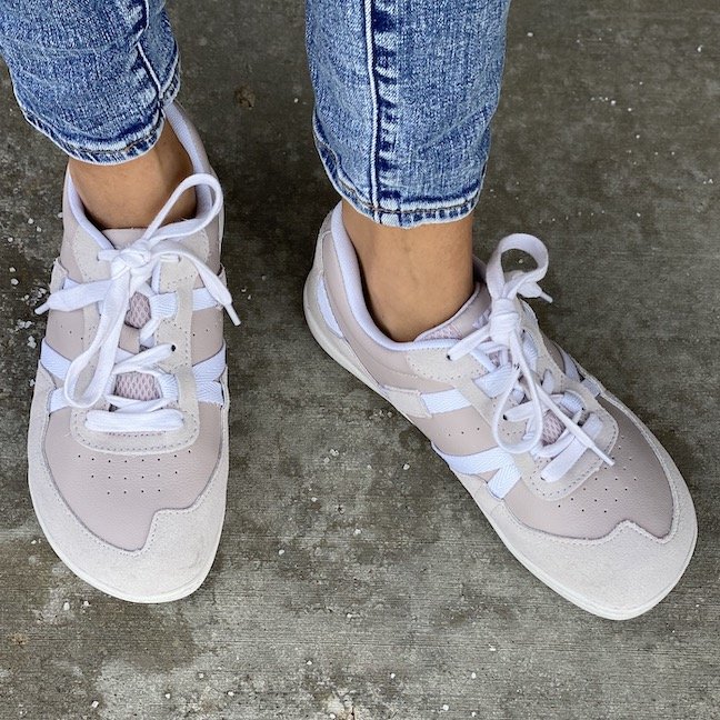 A top down view of a pair of feet standing on concrete wearing the Xero Shoes Kelso barefoot sneaker made of pink leather
