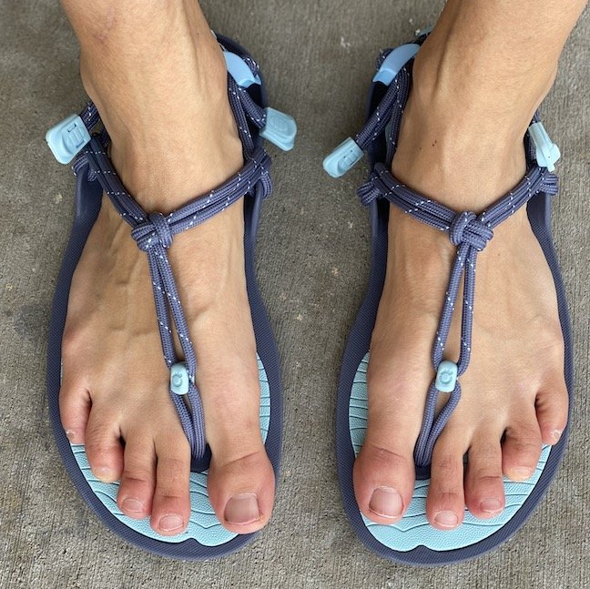 A top down view of a pair of feet standing concrete wearing xero Shoes aqua cloud barefoot sandals