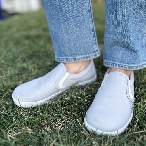 Front and side view of Xero Shoes casual canvas slip ons being worn on green grass with straight leg light colored jeans.
