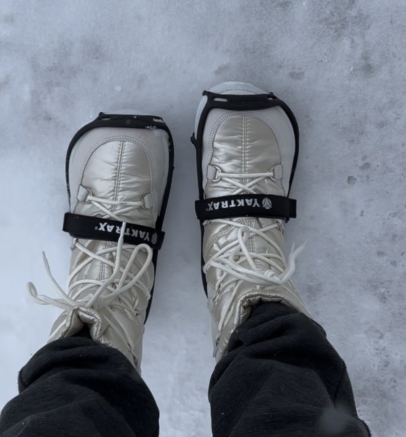 a top down view of a person standing on snow and ice wearing barefoot Be Lenka snowfox winter boots and Yaktrax Ice cleats