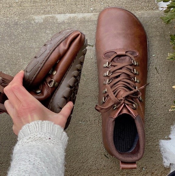 A top down view of a Zaqq Expeq barefoot hiking boot in brown, one is being rolled up to show the flexibility