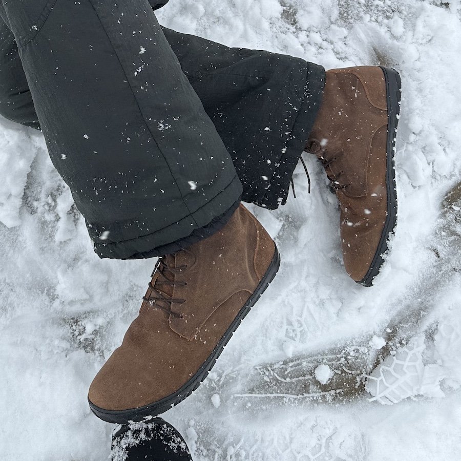 a man laying in the snow wearing Zaqq Quintic warm barefoot winter boots in brown leather with a waterproof finish