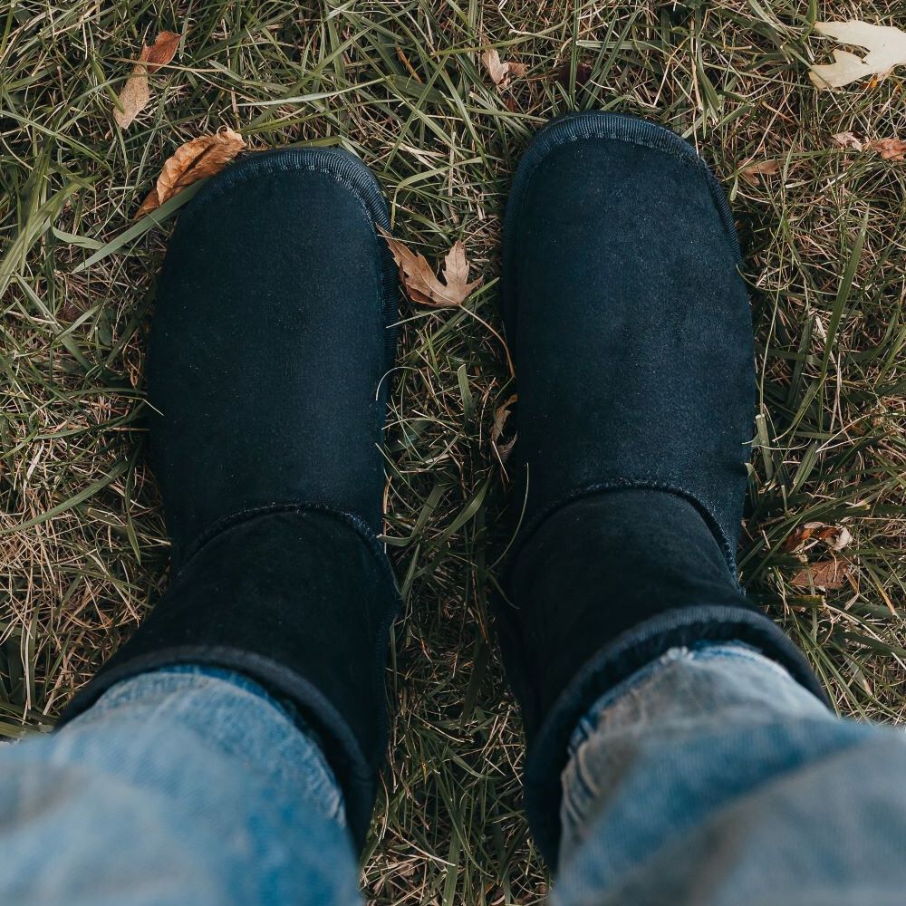 A top down view of a pair of feet standing on grass wearing the Zeazoo Dingo barefoot sheepskin boots in black color