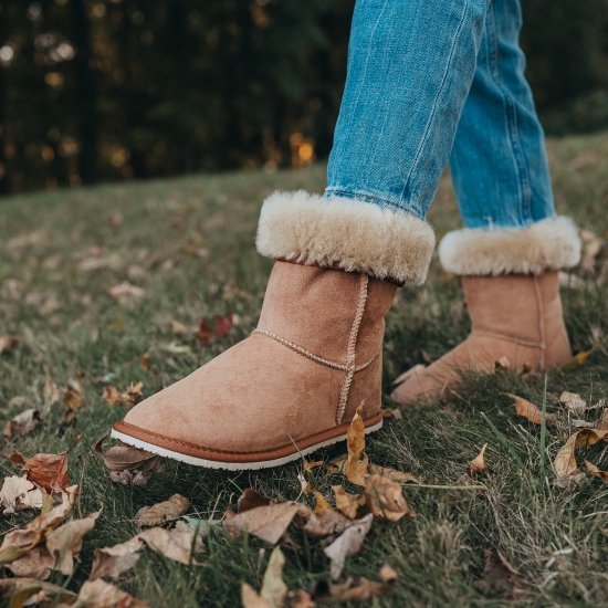 Close up of Zeazoo Dingo Boots in Chestnut brown sheepskin being worn while walking through grass. The white zero drop outsole is visible and the fluffy sheepskin is showing on the turned down cuff