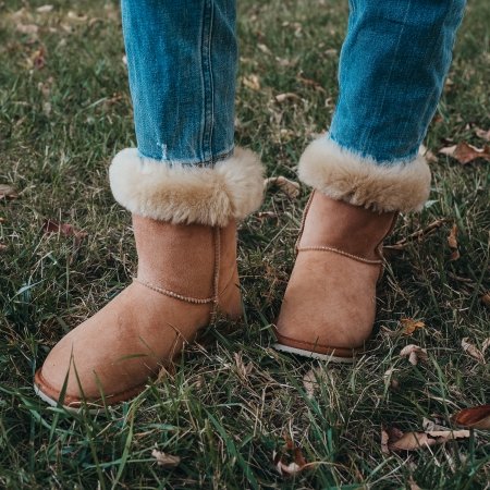 Zeazoo Dingo Chestnut sheepskin winter warm barefoot boots being worn on green grass with jeans. The cuff is turned down to show the plush interior