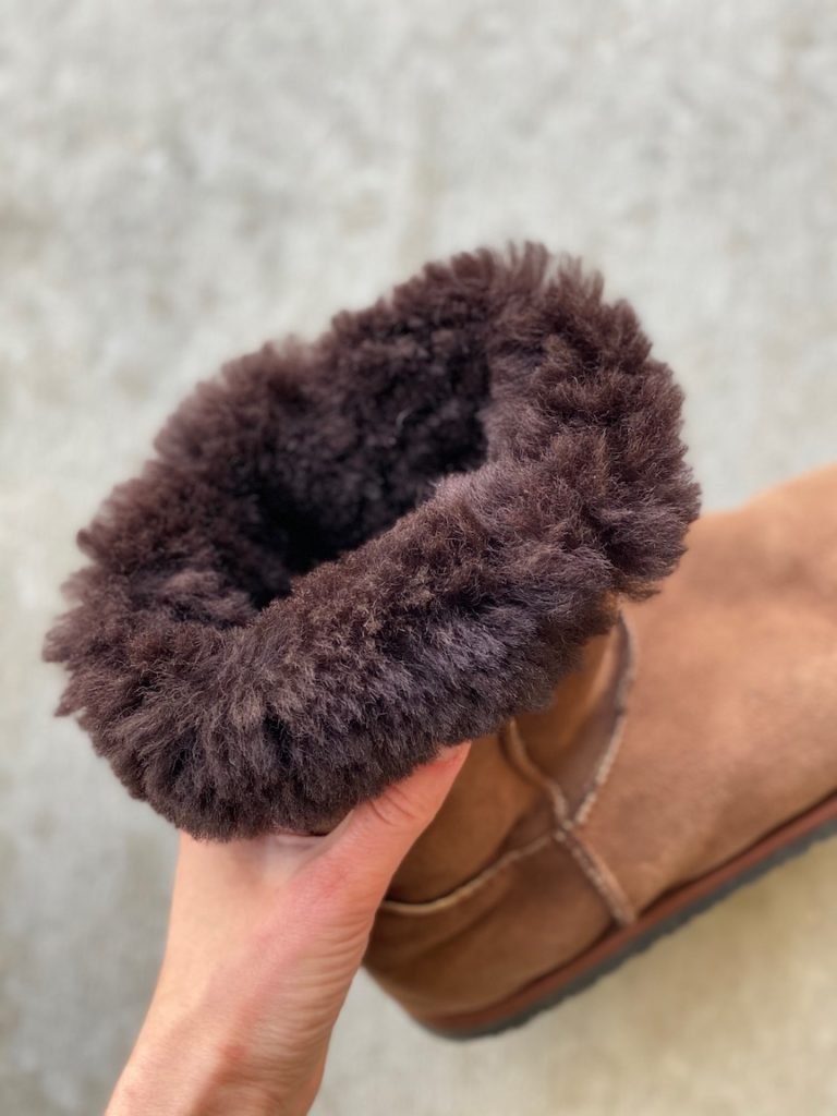 A woman's hand holding the sheepskin cuff on a pair of winter Zeazoo Dingo barefoot boots.