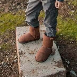 A close up of a child's legs visible from the knees down standing outside wearing Zeazoo Kids Dingo sheepskin barefoot boots